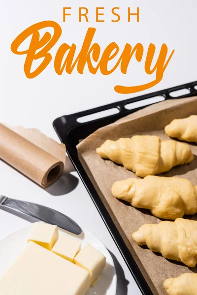 Foyer sélectif de croissants crus sur plaque de cuisson, beurre, couteau près de la boulangerie fraîche lettrage sur blanc — Photo de stock