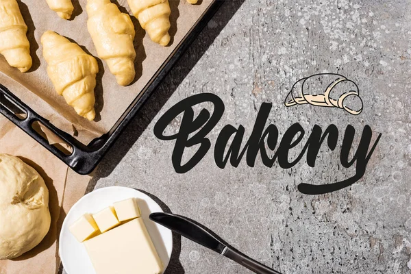 Top view of uncooked croissants on baking tray, dough and butter near bakery lettering on concrete grey surface — Stock Photo