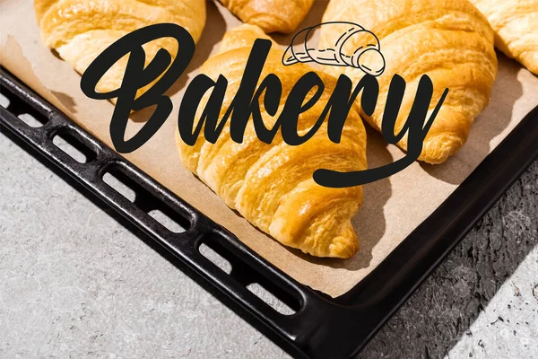 Croissant cotti e deliziosi sulla teglia vicino alla scritta della panetteria sulla superficie grigio cemento — Foto stock