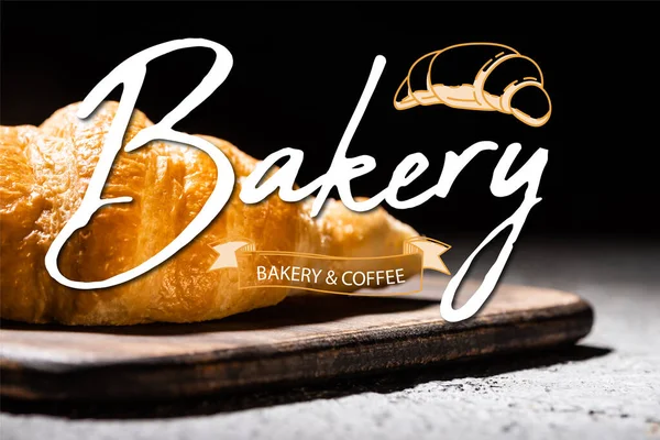 Close up of baked croissant on wooden cutting board near bakery and coffee lettering on black — Stock Photo