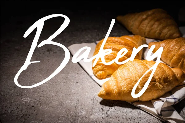 Croissants frescos horneados en la toalla cerca de letras de panadería en la superficie gris de hormigón - foto de stock