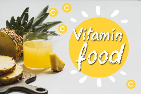 Fresh pineapple juice near sliced fruit on wooden cutting board near vitamin food lettering on white — Stock Photo