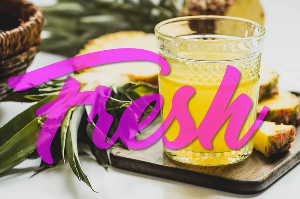 Selective focus of pineapple juice in glass near delicious fruit on cutting board and fresh lettering on white — Stock Photo