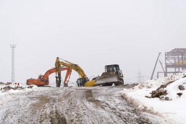 Sovetskaya Gavan, Rusya - 18 Mart 2016: Yoğun kar yağışı altında bir şantiyede sarı ve turuncu ekskavatör ve buldozer