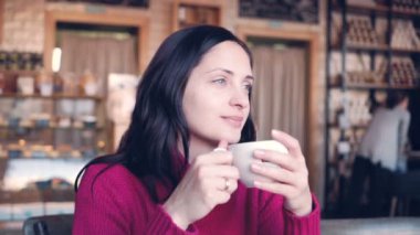 Genç bir kadın bir kafe ve içecek kahve bir masada oturur