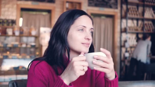 Uma jovem se senta em uma mesa em um café e bebe café — Vídeo de Stock