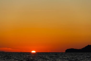 Güneş turuncu gökyüzü ile sahil kenarını gizliyor.