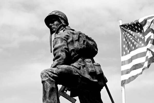 Bronze statue of an Iron Mike, a soldier of the American Army holding a gun with a flag of the United States of America. La Fiere Bridge, Sainte-Mere-Eglise, Normandy, France