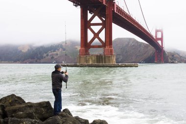 Bir balıkçı Fort Point ön plan üzerinde Golden Gate Köprüsü ile balıkçılık
