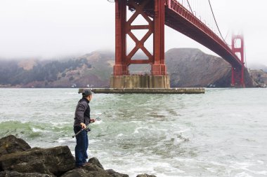 Bir balıkçı Fort Point ön plan üzerinde Golden Gate Köprüsü ile balıkçılık
