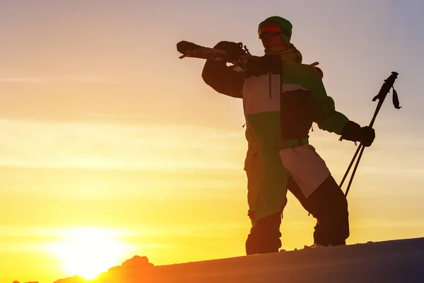 Een skiër houdt ski 's in zijn handen tegen de zonsondergang hemel. — Stockfoto