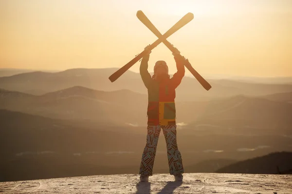 Ein Skifahrer hält Skier in den Händen gegen den Sonnenuntergang. — Stockfoto