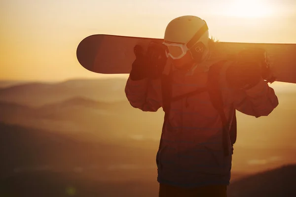 Um jovem no fundo do céu do pôr do sol com um snowboard — Fotografia de Stock