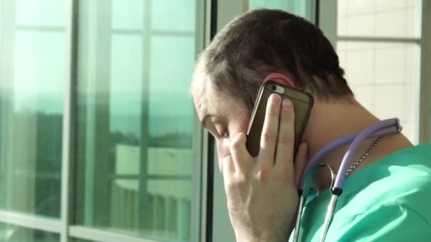 Läkaren är på telefonen vid fönstret — Stockvideo