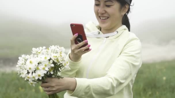 Ασιατικό κορίτσι χαίρεται σκισμένα λουλούδια σε ένα ξέφωτο στην ομίχλη — Αρχείο Βίντεο