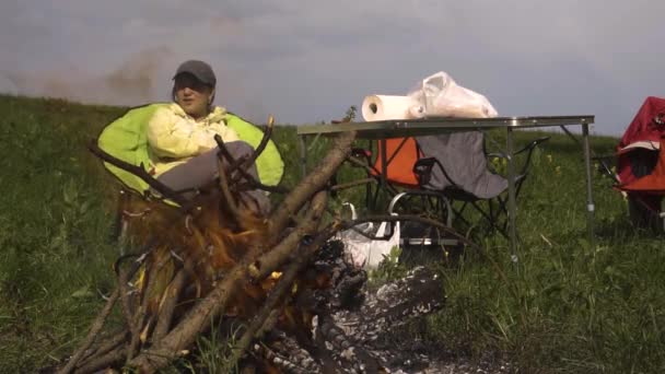 La gente se relaja en la naturaleza alrededor del fuego al atardecer — Vídeos de Stock