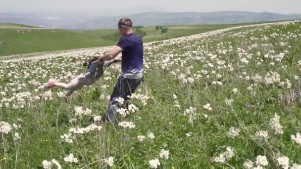 Чоловік обертає свою дочку руками в полі на природі — стокове відео