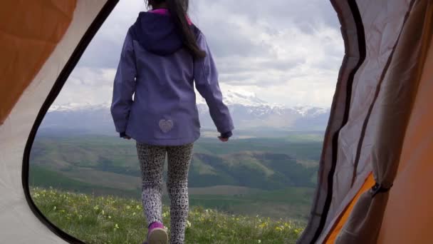 Νεαρή Ασιάτισσα βγαίνει από μια σκηνή στο φόντο των βουνών και ενός ηφαιστείου. — Αρχείο Βίντεο
