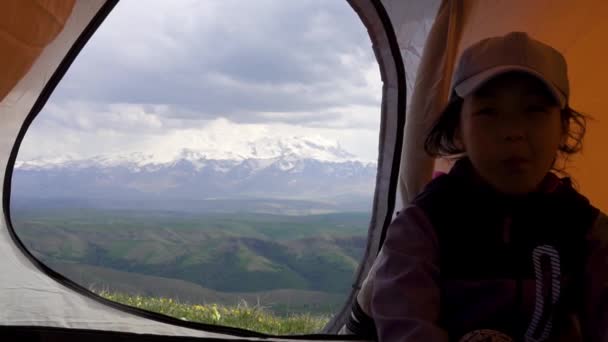 Chica asiática joven sentada en una tienda de campaña en el fondo de las montañas y un volcán — Vídeos de Stock