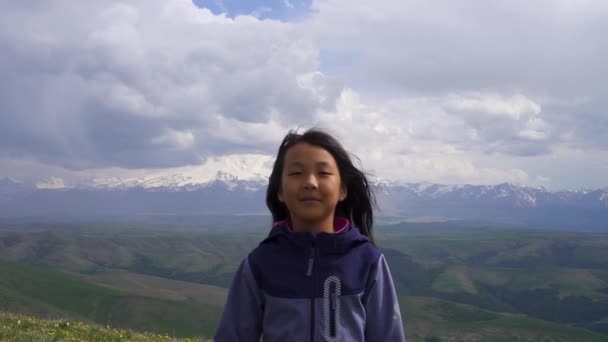 Kleines asiatisches Mädchen, das sich im Wind vor einem Hintergrund von Bergen dreht — Stockvideo