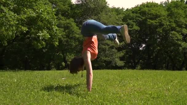 Молодая девушка получает на руки делает расколы в зеленом парке, день — стоковое видео