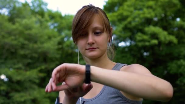 Chica en la naturaleza enciende la música a través del reloj y cierra los ojos — Vídeos de Stock