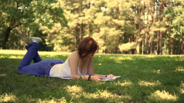 Κορίτσι που βρίσκεται στο γρασίδι στο πάρκο και διαβάζοντας ένα βιβλίο — Αρχείο Βίντεο