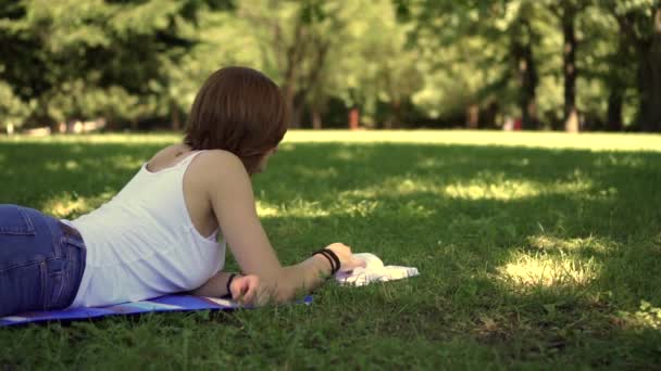 Flicka som ligger på gräset i parken och läsa en bok — Stockvideo