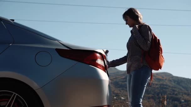 女の子は車のトランクを開けてそこにオレンジのバックパックを置いて — ストック動画