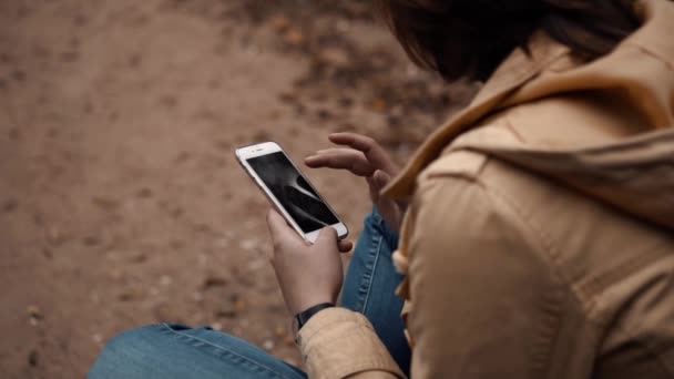 Chica joven sentada sola en un parque con un teléfono — Vídeos de Stock