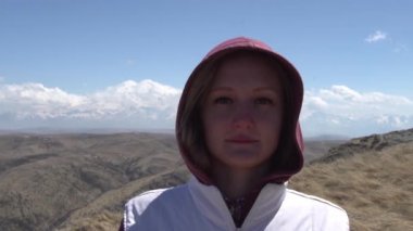 Kız, uyuyan bir volkanın arka planındaki kameraya bakıyor.