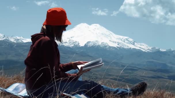 Flicka läser en bok om en bakgrund av berg — Stockvideo
