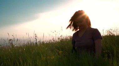 Gün batımında çimenlerde oturan kız.