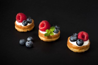 Yaban mersini, ahududu ve siyah arka plan üzerine taze nane ile Belçika Waffle. Makro fotoğraf, portre.