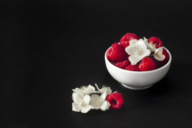 Siyah arka plan üzerine bir kasede beyaz çiçekli taze frambuaz