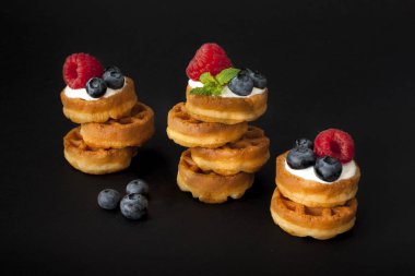 Yaban mersini, ahududu ve siyah arka plan üzerine taze nane ile Belçika waffle yığını. Makro fotoğraf, portre.