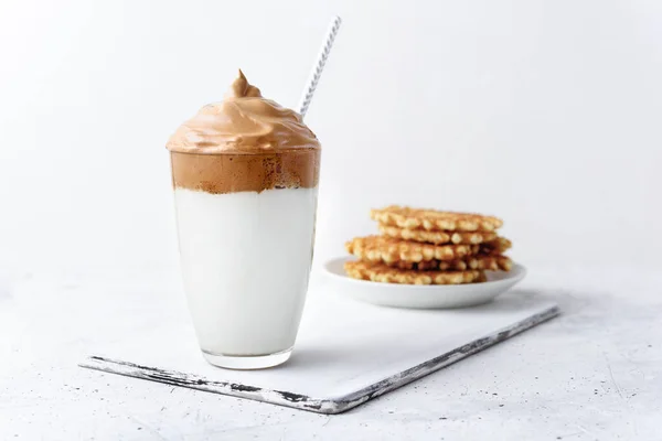 Açık beton arka planda waffle yapan Dalgona kahvesi. İçeceği ve kağıt tüpü olan şeffaf camlar. Ev yapımı Moda Kore kahvesi, soğuk içecek, çırpılmış kahve ve süt. Boşluğu kopyala