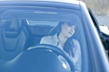 Güzel esmer kız siyah cabriolet oturur, araba iç deri, siyah. Görünümü izleyiciye yöneliktir. Mavi ranzada. Kız üzgün.