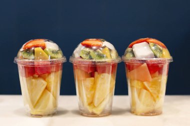Plastik cam üç karışık meyve vitamin salatası paket hazır. Kivi, ananas, karpuz, hindistan cevizi, çilek, plastik kapta mango. Kopyalama alanı.