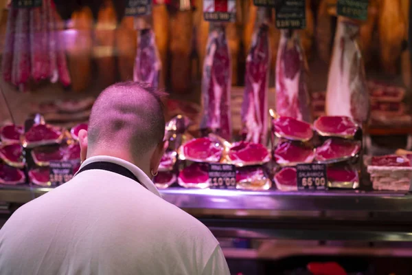 Junger glatzköpfiger Metzger schneidet Fleisch mit dem großen Spezialmesser auf dem berühmten Markt in Barcelona, Katalonien, Spanien 2019-04-30 — Stockfoto