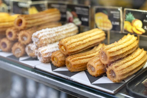 Diferentes tipos de churros tradicionales de postre dulce español con relleno en el mercado o escaparate de panadería. Plato de pastelería caliente . — Foto de Stock