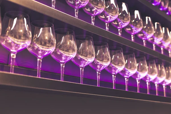 Estante con un montón de copas de vino vacías con luz rosa y violeta. Bar o interior de la tienda de cristalería. Concepto de celebración, evento o fiesta . —  Fotos de Stock