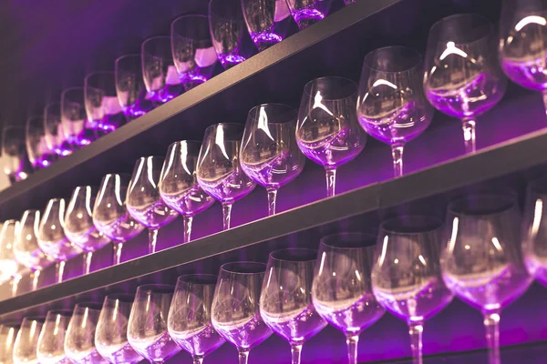 Półka z wieloma pustymi kieliszkami do wina z różowym i fioletowym światłem. Bar lub szklane wnętrze sklepu. Koncepcja obchodów, imprez lub imprez. — Zdjęcie stockowe