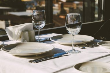 Restoranda masa ayarı. Boş şarap bardakları, tabaklar, çatallar, masa örtüsündeki bıçaklar. Zarif restoran iç.