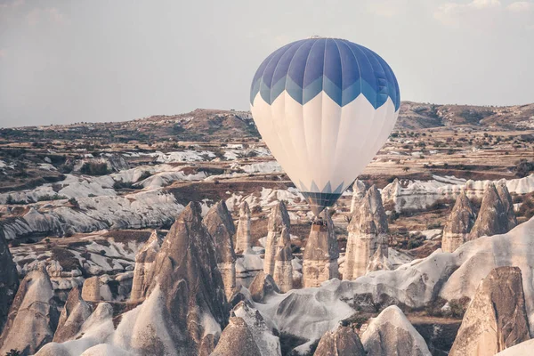 Landscape with hot air balloon that flying low over the mountains. Famous Turkish region Cappadocia with mountains and cave cities.