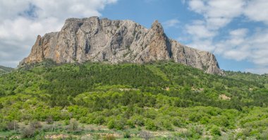 Yeşil vadiden daha yüksek kayalar. Ağaçların arasına gizlenmiş bir yol. Güzel bulutları ve güneşli bir günü olan güzel bir manzara. Krim