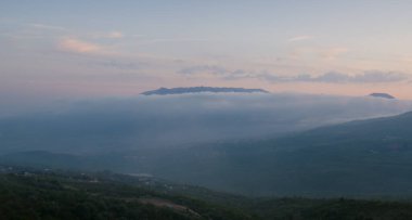 Akşam alacakaranlığında sis dağları kaplar, Kırım. Issız yol tepeye tırmanır, evler yeşilde kaybolur. Huzurlu bir akşam vadisi, Güney Kırım 'ın doğal manzarası..