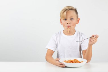 little blond boy in front of white background eats spaghetti and smiles