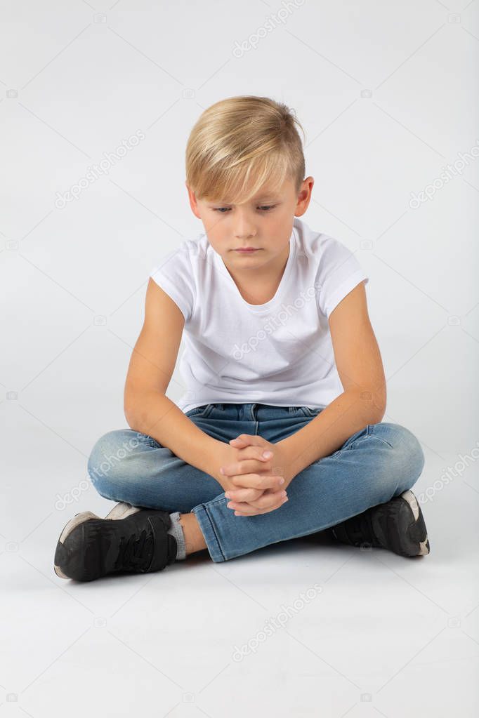 little blond boy is sitting sadly on the floor white background