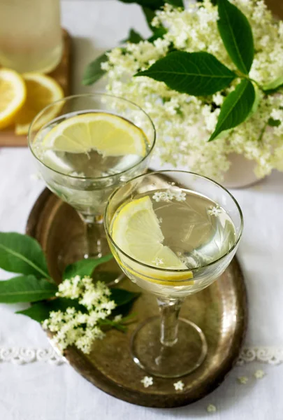 A cool drink with lemon and elderflower syrup in glasses on a metal tray. Rustic style, selective focus.
